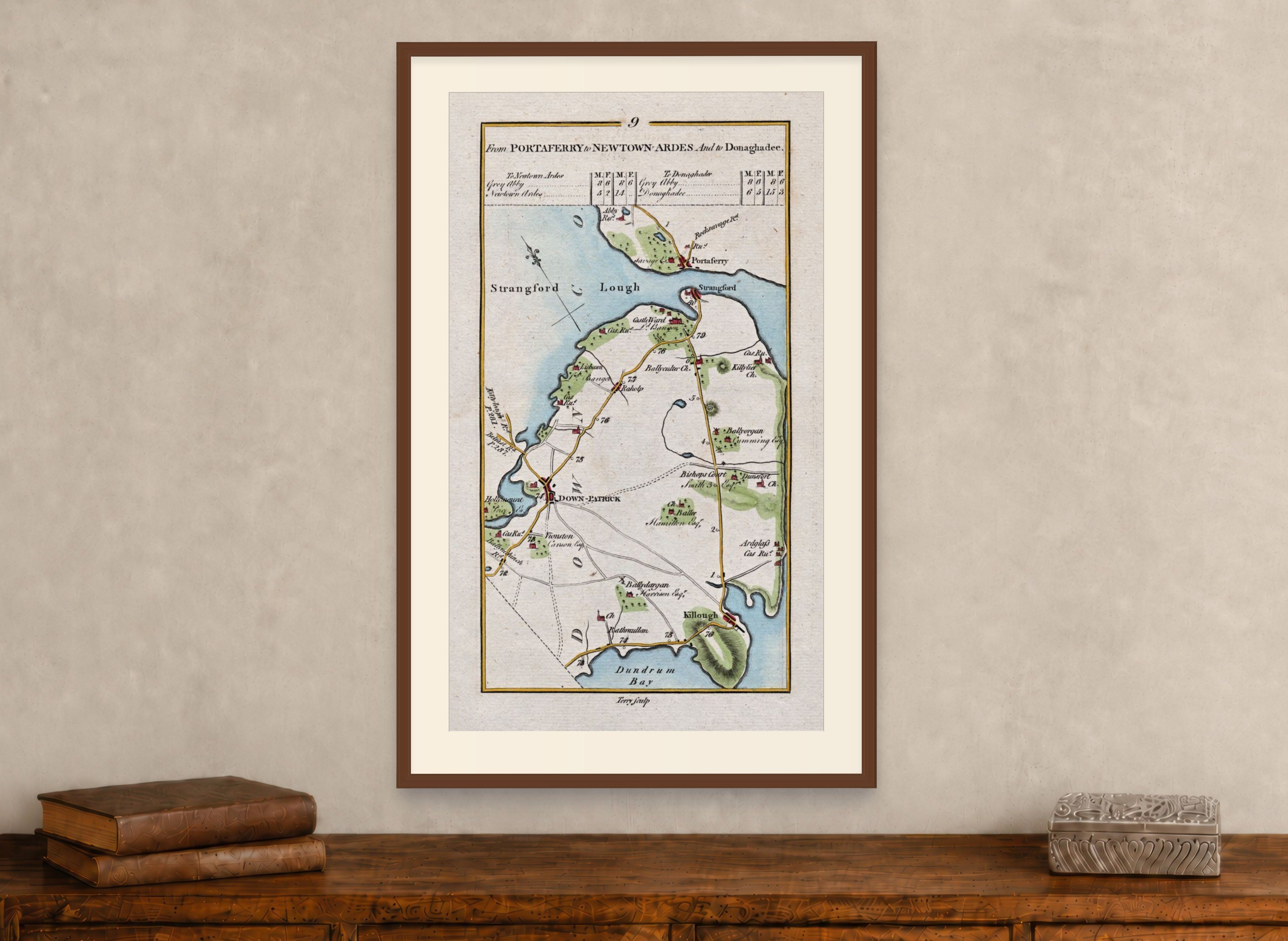 Framed 1783 Taylor & Skinner Ireland road map showing Downpatrick, Strangford, Portaferry and Killough, displayed above an antique wooden cabinet.