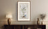 Framed antique Ireland road map displayed above a dark wooden cabinet with a lamp and decorative vase.