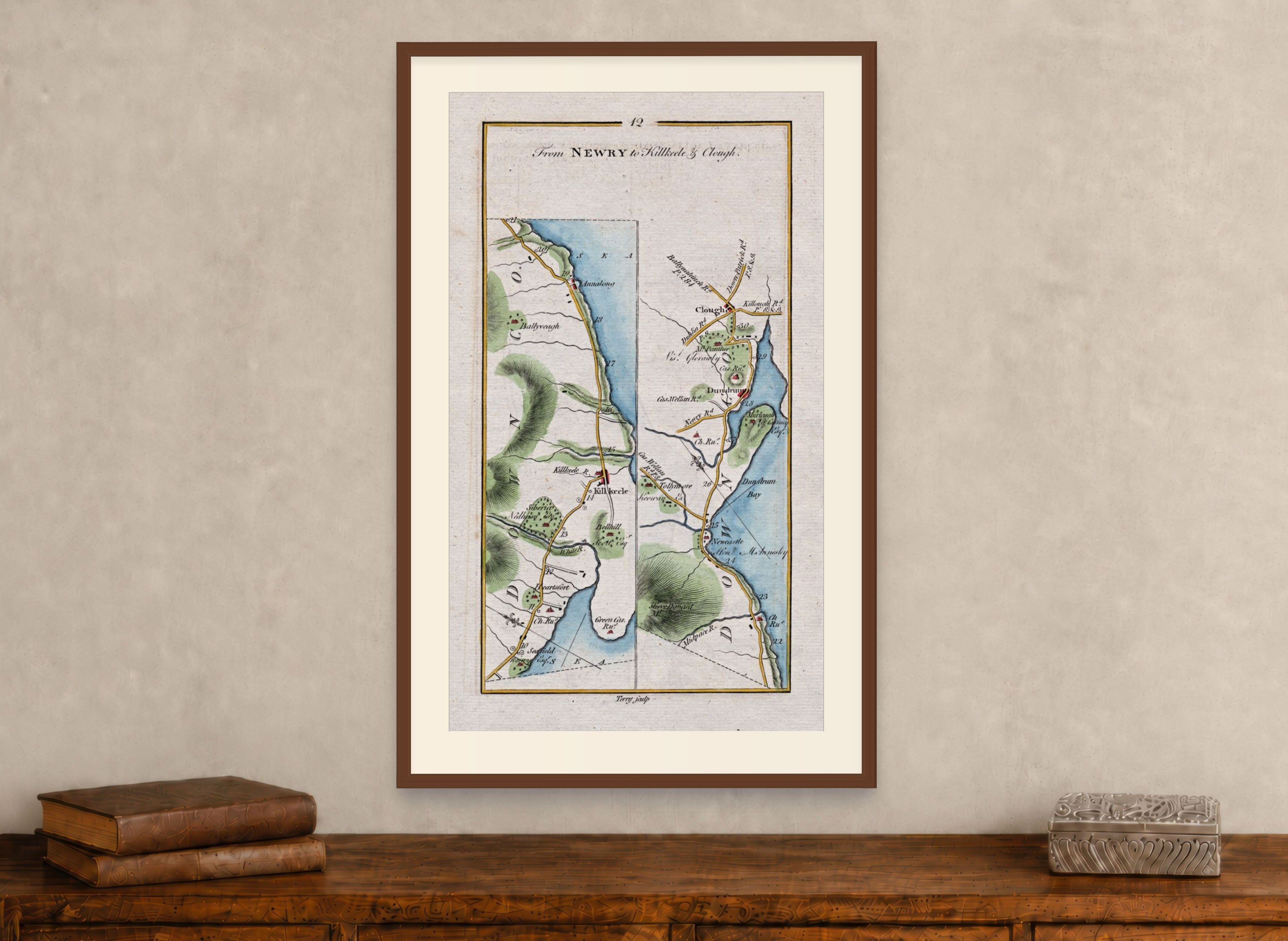 Framed 1783 Taylor & Skinner Kilkeel, Newcastle, Dundrum, Annalong and Clough, Ireland road map displayed above an antique wooden cabinet.