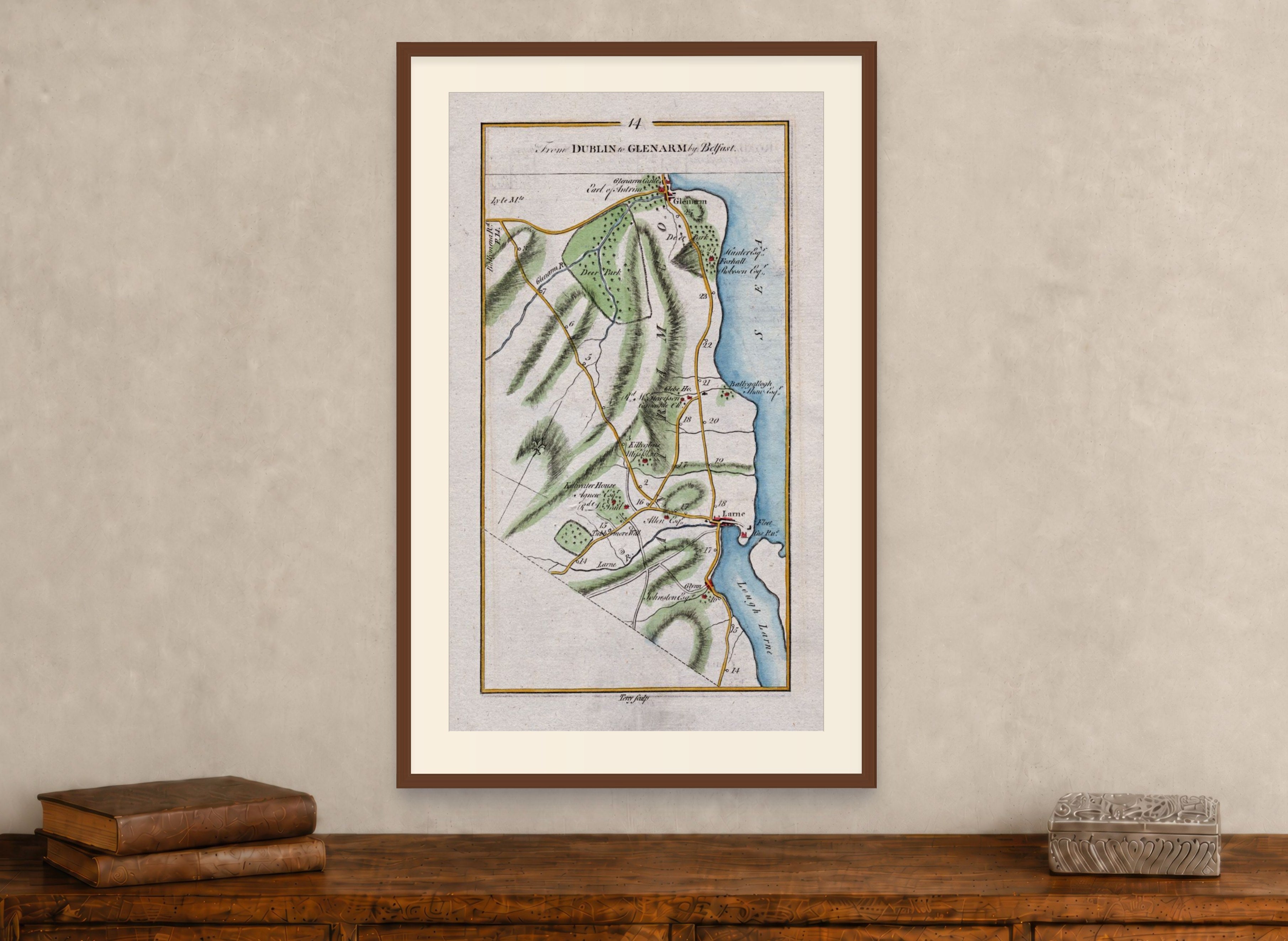 Framed 1783 Taylor & Skinner Larne, Glenarm, Ballygally and Glynn, Ireland road map displayed above an antique wooden cabinet.