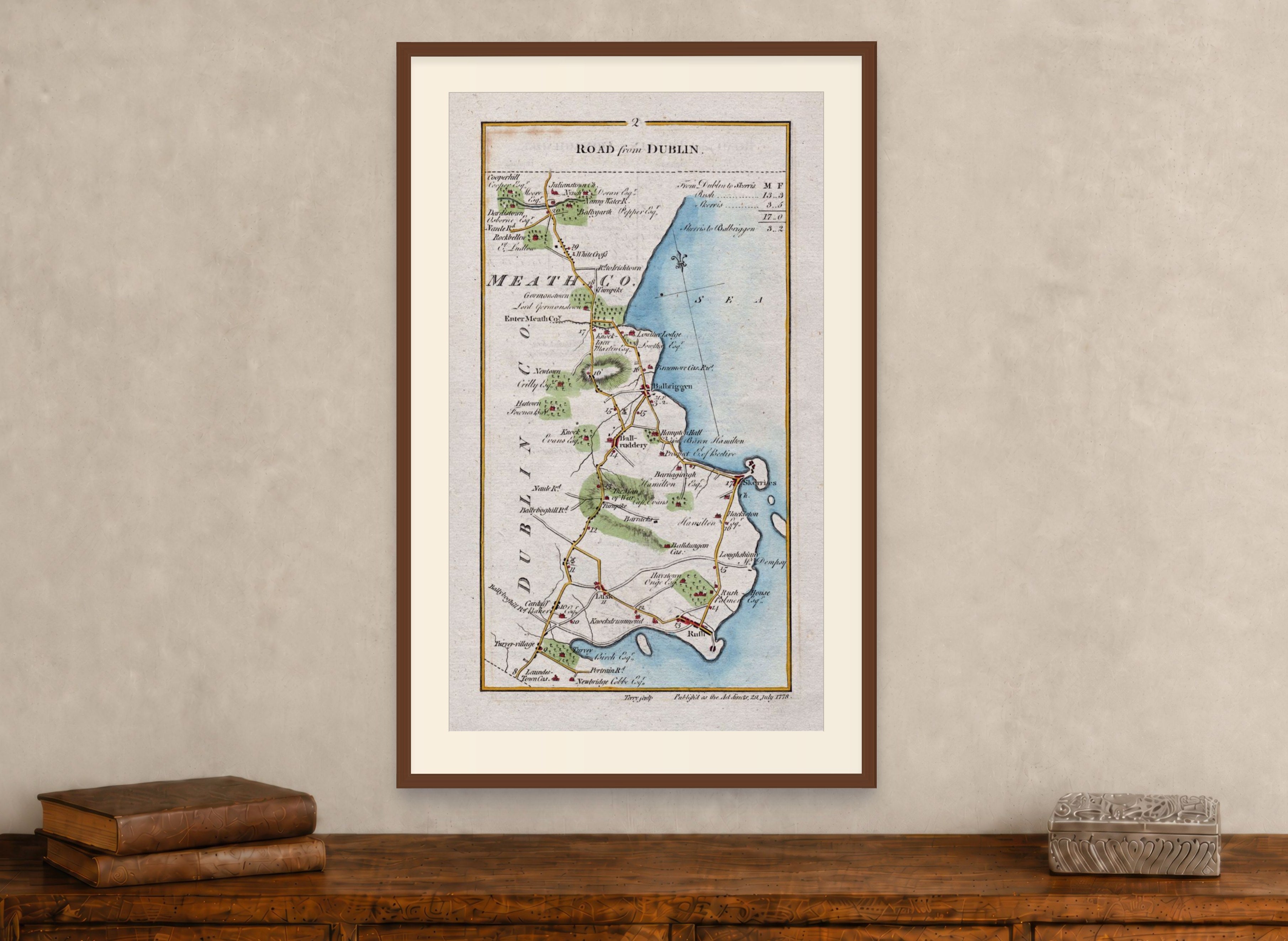 Framed 1783 Taylor & Skinner Lusk, Rush, Skerries and Balbriggan road map displayed above an antique wooden cabinet.