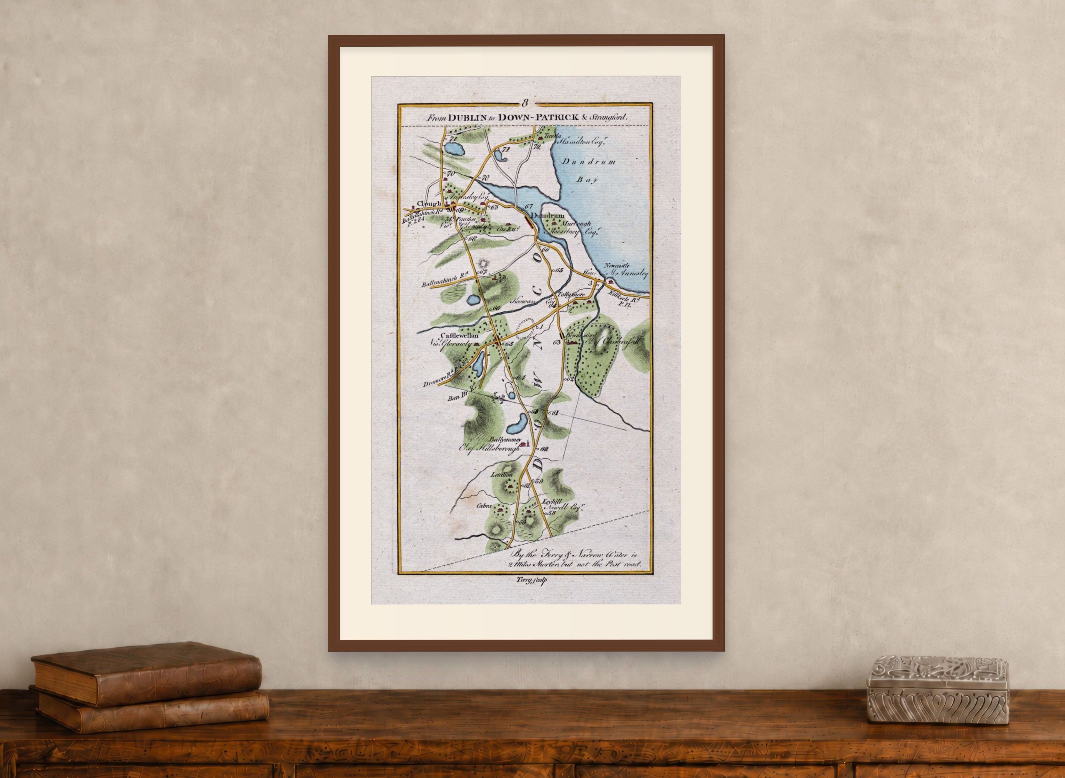 Framed 1783 Taylor & Skinner Ireland road map showing Newcastle, Castlewellan, Dundrum and Clough, displayed above an antique wooden cabinet.