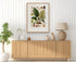 1879 Anthurium malyi antique botanical print, Plate 10 by Heinrich Wilhelm Schott, framed above a natural oak sideboard in a bright, neutral living room.