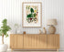 1879 Syngonium riedelianum antique botanical print, Plate 18 by Heinrich Wilhelm Schott, framed above a natural oak sideboard in a bright, neutral living room.